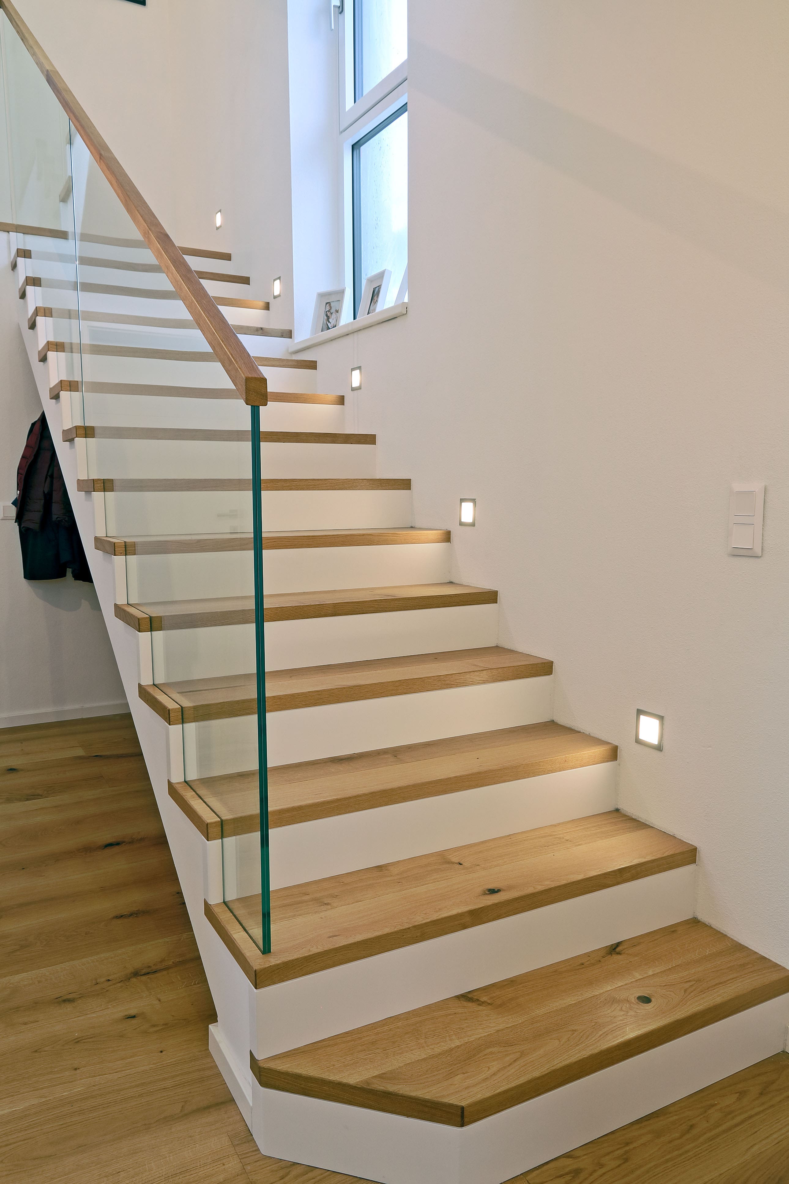 Moderne Holztreppe mit weißen Setzstufen und Glasgeländer